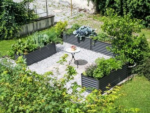 A garden patio with a round table and benches, surrounded by raised planters and a gravel path. - Apartment Frieda by Interhome (Landeck)