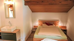 A bedroom with a wooden ceiling, a bedside table with a lamp, a bed with a pillow, and a small stool. - Apartment Frieda by Interhome (Landeck)