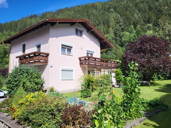 Ein zweistöckiges Haus mit Balkon, umgeben von einem Garten mit verschiedenen Pflanzen und Blumen.