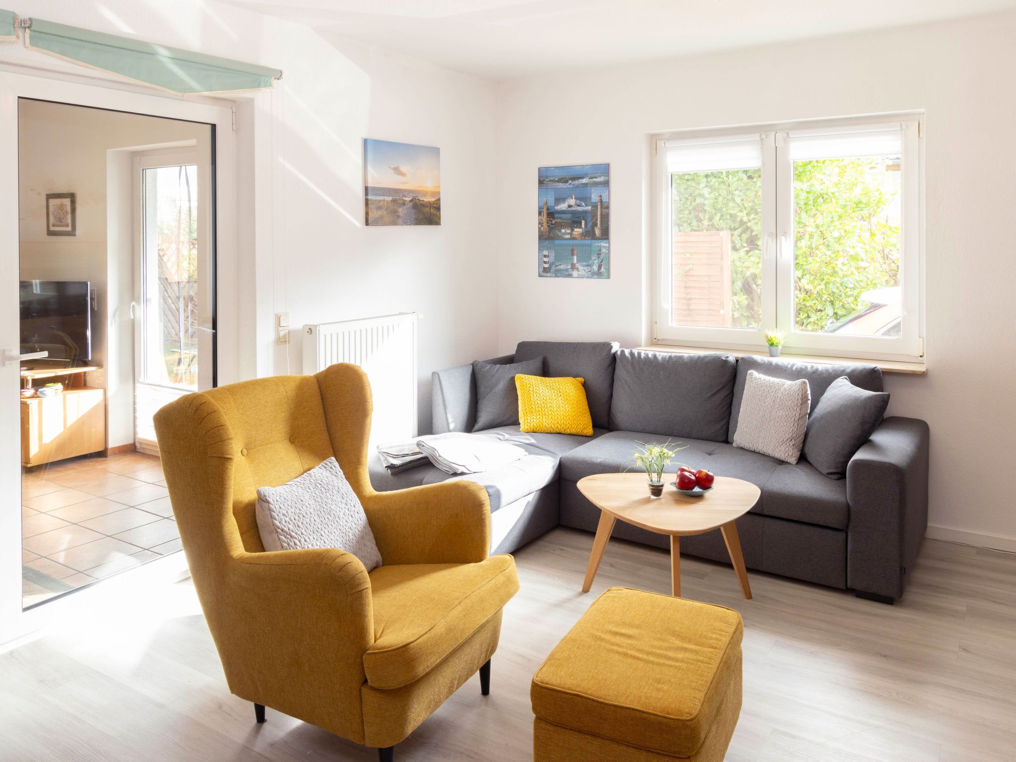 A living room with a sofa, armchair, ottoman, and a small table. There is a window with a view of greenery outside.