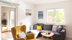 A living room with a sofa, armchair, ottoman, and a small table. There is a window with a view of greenery outside. - Vacation home Enikö by Interhome (Ostseebad Lubmin)