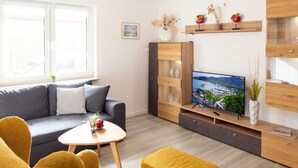 A modern living room with a grey sofa, yellow armchairs, a wooden TV stand, and a small round table with a vase and fruit. - Vacation home Enikö by Interhome (Ostseebad Lubmin)