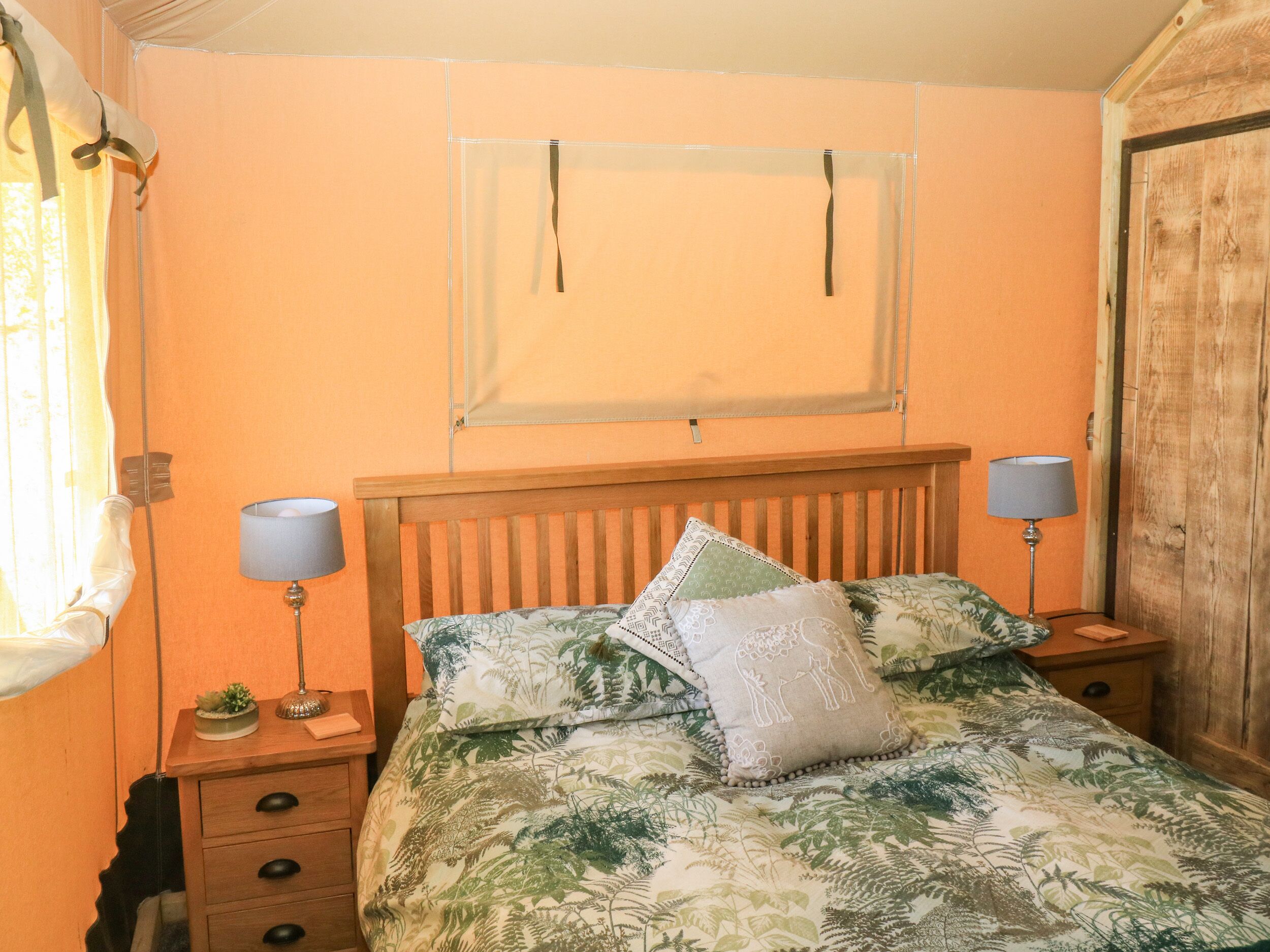 A bedroom with a bed, two bedside tables, a nightstand, a window with curtains, and a wooden door.