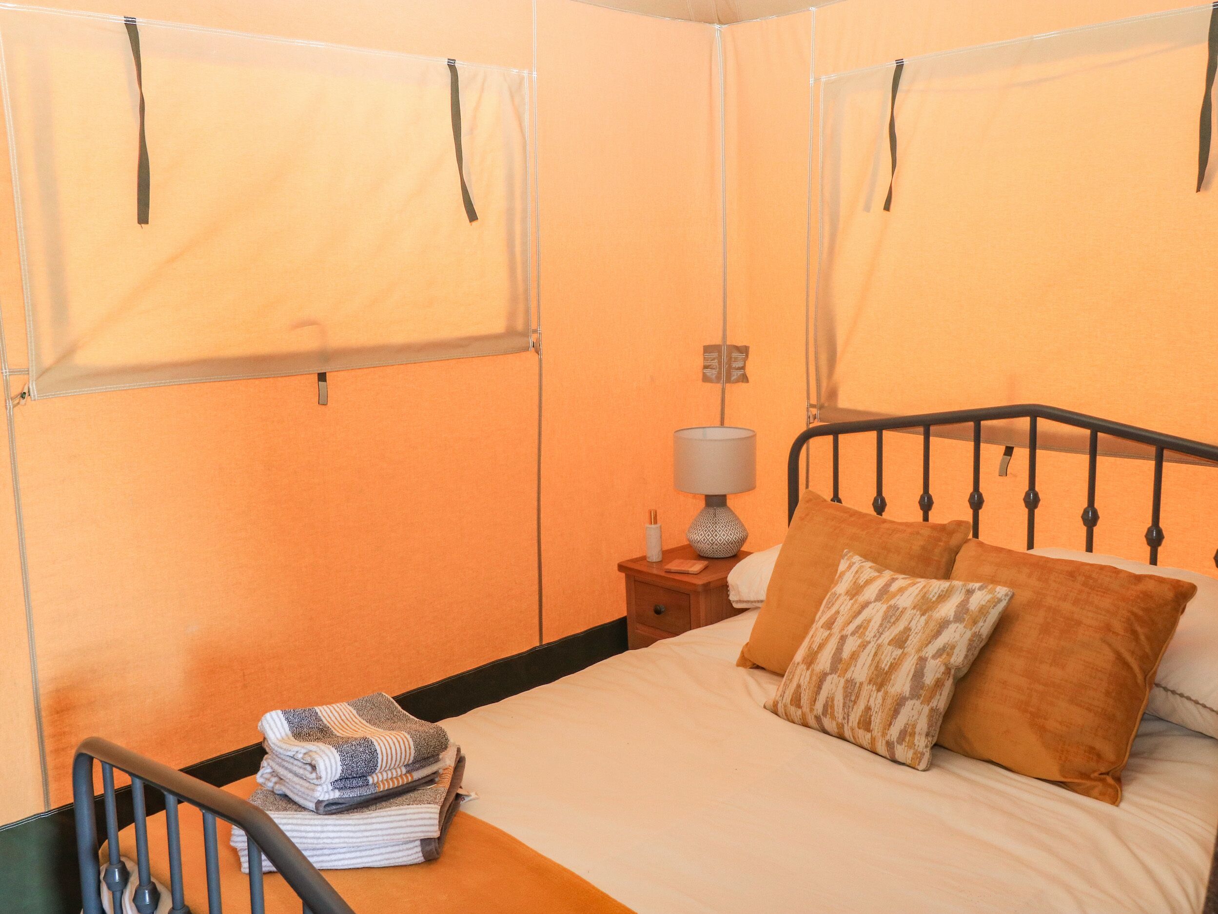 Uma cama de solteiro com cabeceira, mesa de cabeceira com abajur e uma pilha de toalhas.