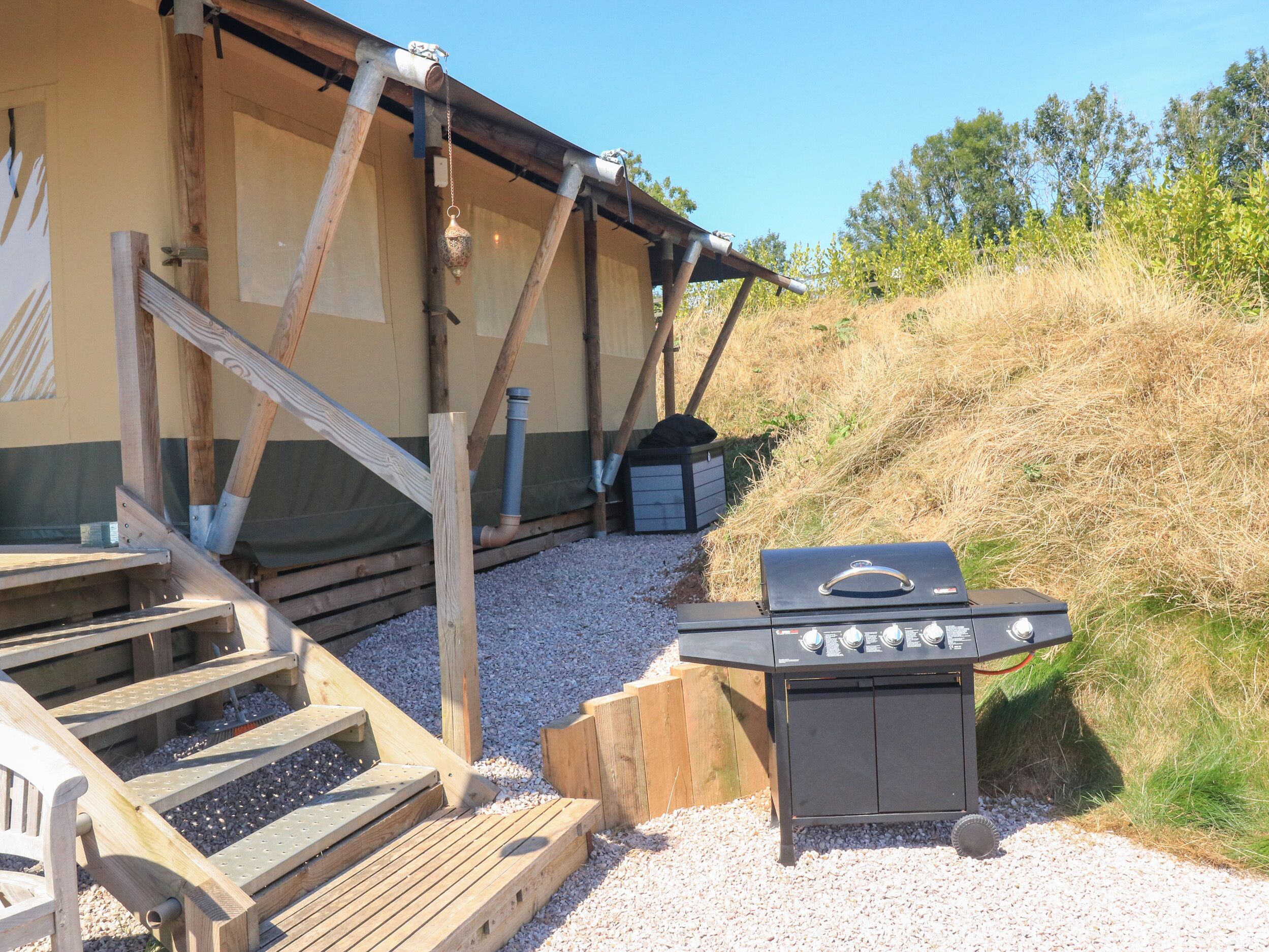 Eine Holzterrasse mit Grill, einer Holzbank und einem kleinen Schuppen.