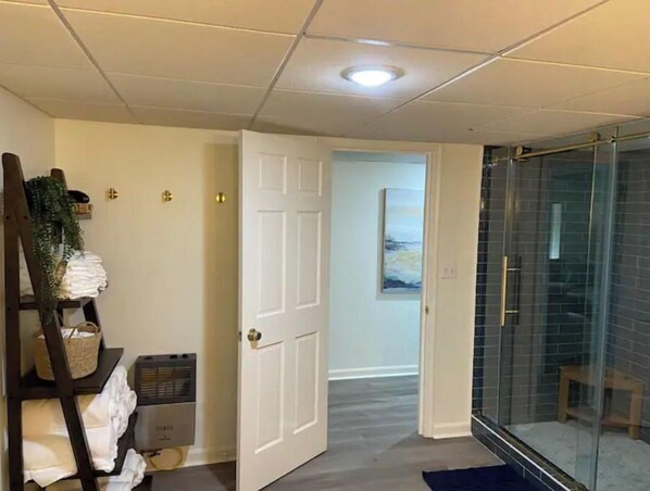 Habitación de hotel con zona de ducha, una puerta que da a otra habitación y un pequeño banco cerca de la ducha.