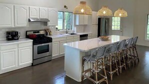 Una cocina moderna con armarios blancos, electrodomésticos de acero inoxidable, una isla central con taburetes de bar e iluminación colgante.