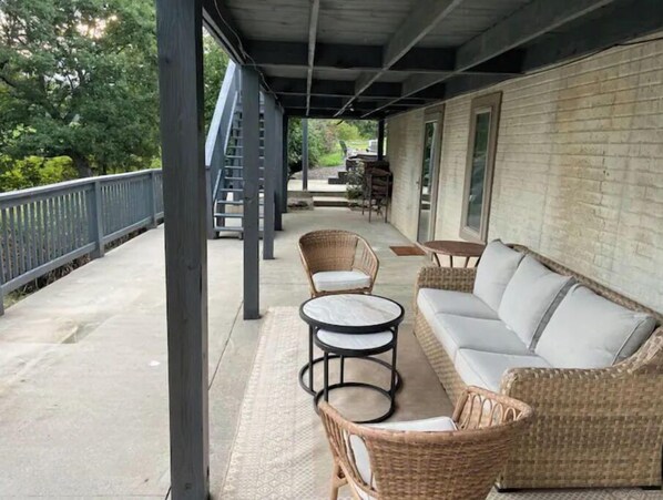 A covered outdoor area with wicker furniture, a staircase, and a brick wall.