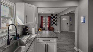 Una cocina con armarios blancos, encimera de granito, pileta de acero inoxidable y una cafetera.