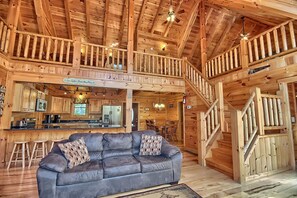 A spacious cabin interior with a wooden staircase, a kitchen area, and a seating area with a sofa.