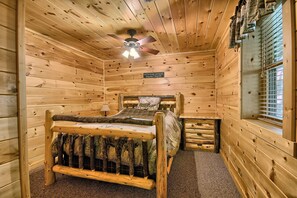 A wooden cabin room with a bed, a nightstand, a window with blinds, and a ceiling fan.