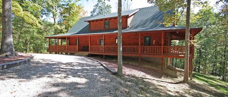 A two-story log cabin with a porch and a covered deck, surrounded by trees.