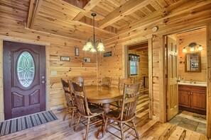 A wooden interior with a dining table and chairs, a chandelier, and a kitchen area. - Hidden Valley Lodge, 8-BedRm Lodge - Hocking Hills (Logan)