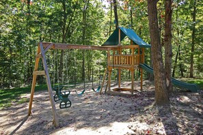 A wooden swing set with a slide, surrounded by trees. - Hidden Valley Lodge, 8-BedRm Lodge - Hocking Hills (Logan)