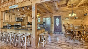 Interno di una baita in legno con angolo cottura, bancone e zona pranzo.