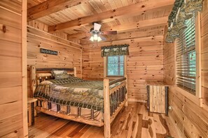 Ein Schlafzimmer einer Holzhütte mit einem Bett, einem Deckenventilator, einem Fenster mit Jalousien und einem Schild an der Wand.