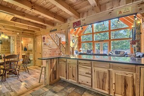 A wooden cabin interior with a kitchen area, wooden dining table, and a staircase leading to a balcony. - Hidden Valley Lodge, 8-BedRm Lodge - Hocking Hills (Logan)