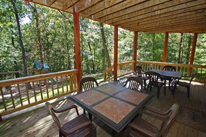 Eine hölzerne Terrasse im Freien mit Tisch und Stühlen, umgeben von Bäumen.