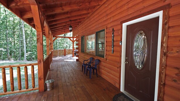 A wooden cabin with a porch, a welcome sign, and a door with a glass panel. - Maple Ridge Lodge - 5-Bedroom Lodge -Hocking Hills (South Bloomingville)