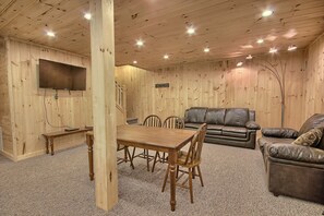 Um interior em madeira com uma mesa de jantar, cadeiras, um sofá de couro e uma televisão fixada na parede.