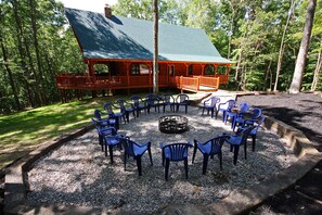A lodge with a covered deck and outdoor seating area with chairs arranged around a fire pit.