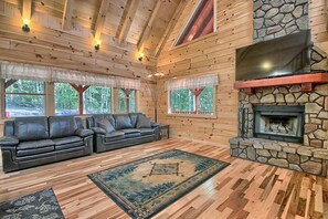 A log cabin interior with a stone fireplace, leather sofas, and large windows. - Maple Ridge Lodge - 5-Bedroom Lodge -Hocking Hills (South Bloomingville)