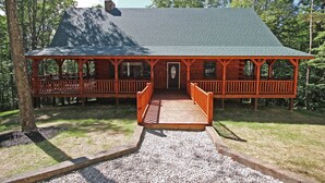 A wooden cabin with a porch, a covered deck, and a gravel pathway leading to the entrance. - Maple Ridge Lodge - 5-Bedroom Lodge -Hocking Hills (South Bloomingville)