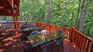 An outdoor deck with tables and chairs, surrounded by a wooden railing, overlooking a forested area. - Maple Ridge Lodge - 5-Bedroom Lodge -Hocking Hills (South Bloomingville)