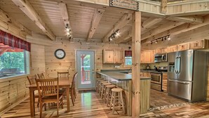 A wooden cabin-style kitchen with a dining area, wooden flooring, and a bar counter. - Maple Ridge Lodge - 5-Bedroom Lodge -Hocking Hills (South Bloomingville)