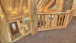 Interior de una cabaña de madera con pared de piedra, escalera de madera y un letrero de cabaña.