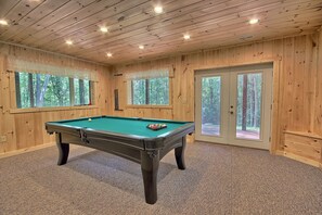 A pool table in a room with wooden walls and large windows.