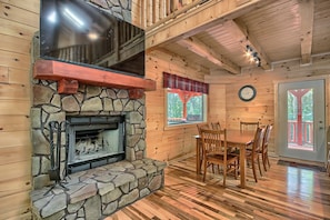 A cozy cabin interior with a stone fireplace, wooden dining table, and a large TV mounted on the wall. - Maple Ridge Lodge - 5-Bedroom Lodge -Hocking Hills (South Bloomingville)