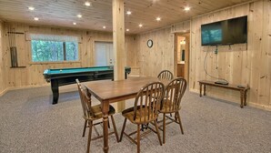 A wooden-paneled room with a pool table, chairs, a television, and a clock. - Maple Ridge Lodge - 5-Bedroom Lodge -Hocking Hills (South Bloomingville)