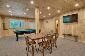 Une pièce aux murs lambrissés, équipée d’une table de billard, de chaises, d’un téléviseur et d’une horloge.