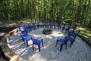A circular arrangement of blue plastic chairs around a central fire pit in a forested area. - Maple Ridge Lodge - 5-Bedroom Lodge -Hocking Hills (South Bloomingville)