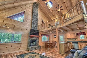 A cabin interior with a stone fireplace, wooden floors, a dining area, and a kitchen. - Maple Ridge Lodge - 5-Bedroom Lodge -Hocking Hills (South Bloomingville)