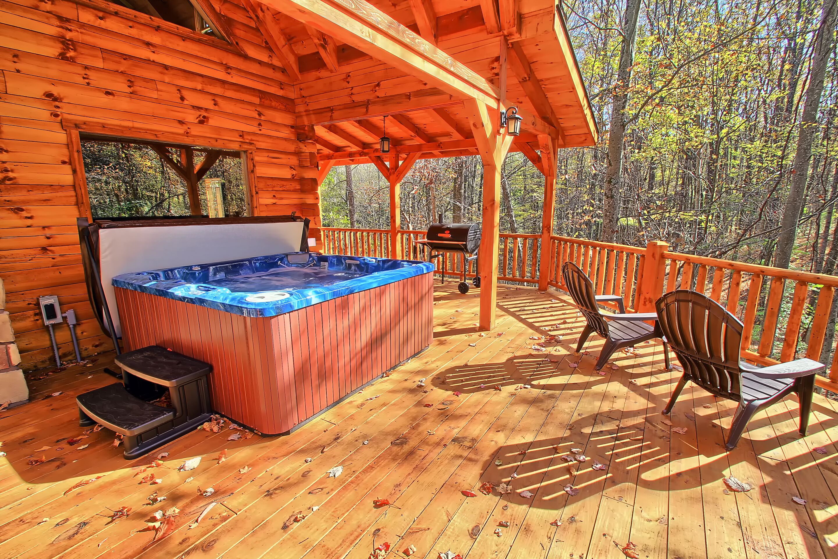 Een houten terras met een jacuzzi, buitenmeubilair en uitzicht op het bos.