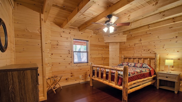 A wooden cabin room with a bed, a nightstand, a window, and a ceiling fan. - Dogwood Lane Lodge- sleeps up to 18 -Hocking Hills (Logan)