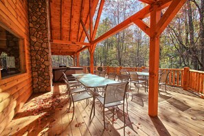 Une terrasse extérieure couverte, dotée d’un mur en pierre, de poutres en bois et d’une table avec des chaises.