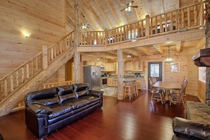 Ein Holzblock-Interieur mit Ledersofa, einem Esstisch mit Stühlen, einer Küchenzeile und einer Treppe, die zu einer oberen Ebene führt.