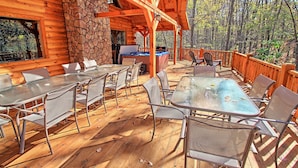 An outdoor patio with wooden tables and chairs, a stone wall, and a view of a forest. - Dogwood Lane Lodge- sleeps up to 18 -Hocking Hills (Logan)