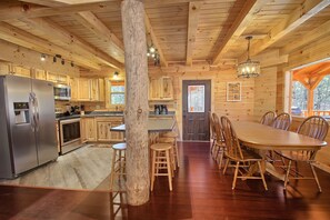 A wooden cabin interior with a kitchen, dining area, and a large wooden post. - Dogwood Lane Lodge- sleeps up to 18 -Hocking Hills (Logan)