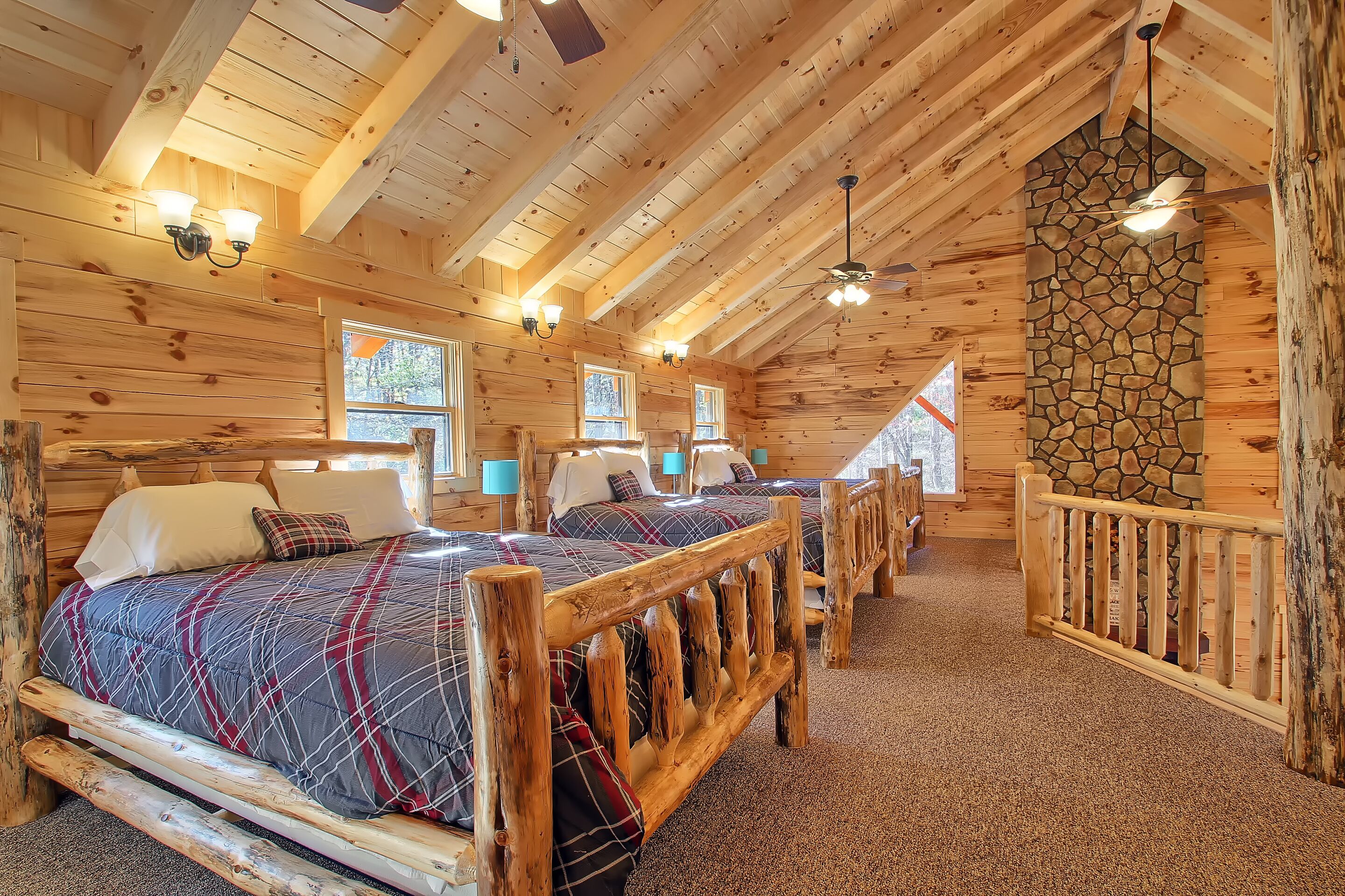 A log cabin bedroom with a large bed, two bedside tables, a stone fireplace, and a view of the outdoors.