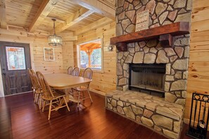Un intérieur en bois avec une cheminée en pierre, une table à manger avec des chaises et une grande fenêtre.