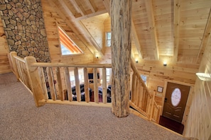 Un interior de madera con una pared de piedra, una escalera de madera y una puerta con un ventanal circular.