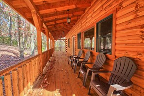 Une cabane en bois dotée d’un porche, d’une terrasse en bois et de fauteuils Adirondack.