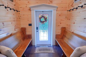 Una cabaña de madera con puerta principal, bancos y felpudo.