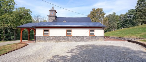 A two-story building with a stone facade and a metal roof, featuring a covered porch and a gravel driveway.