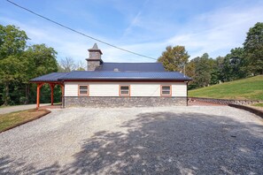 A two-story building with a stone facade and a metal roof, featuring a covered porch and a gravel driveway.