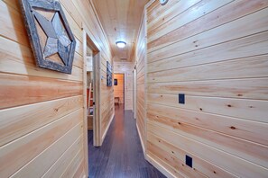 A wooden hallway with a geometric wall decoration, a door leading to another room, and a ceiling light fixture. - Chapel Valley Lodge - Unique, in the Hocking Hills (Logan)